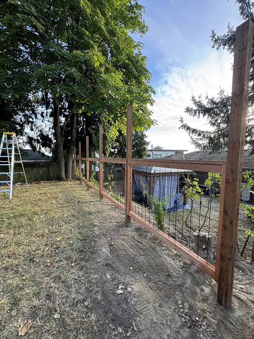 Hog wire panels being attached between fence posts in the lower portion of the fence